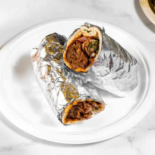 Two Indian burritos, wrapped in foil and cut in half, revealing meat and vegetables on a white plate.