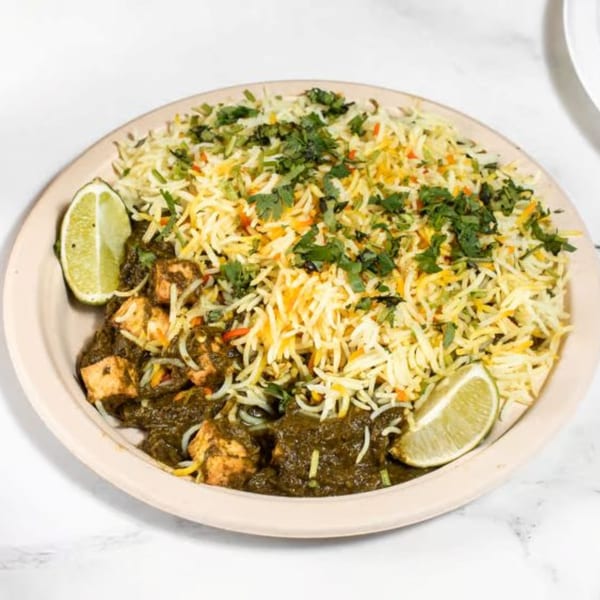 Indian palak paneer with basmati rice and lime wedges in a light brown bowl.