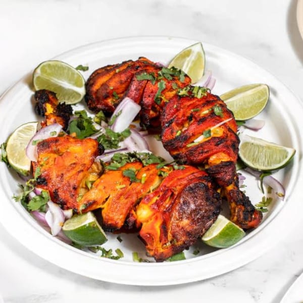 Tandoori chicken drumsticks and thighs, garnished with lime wedges, red onions, and cilantro.