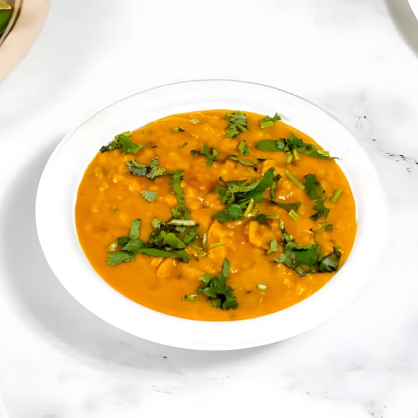A white bowl filled with orange Indian dal, garnished with fresh green cilantro, on a white marble surface.