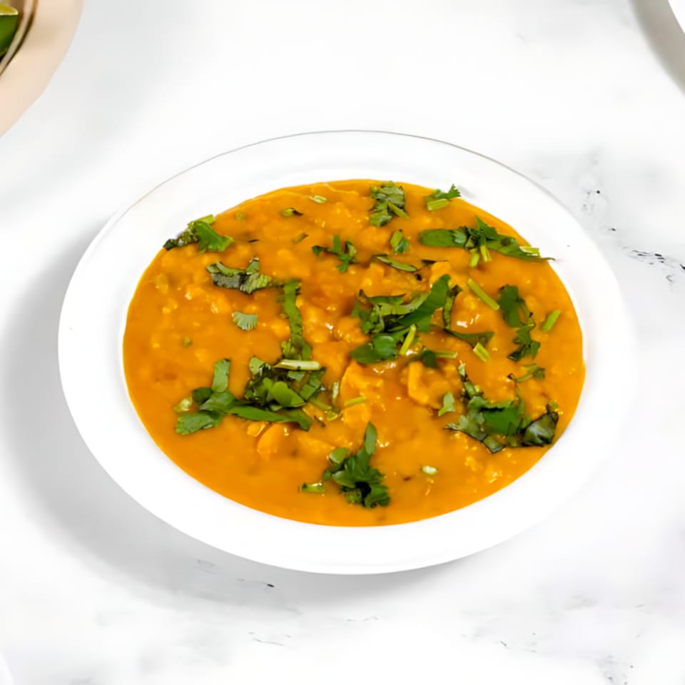 A white bowl filled with orange Indian dal, garnished with fresh green cilantro, on a white marble surface.