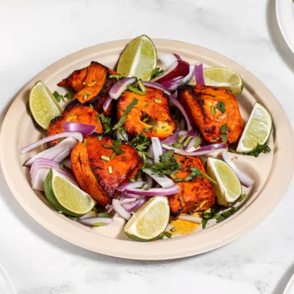 Indian chicken tikka, garnished with red onions, cilantro, and lime wedges on a plate.